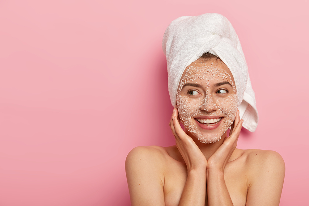 pleased-young-woman-with-delighted-expression-applies-natural-beauty-product-face-uncloges-pores-has-charming-smile-looks-aside-has-wrapped-towel-head-has-naked-body-healthy-skin